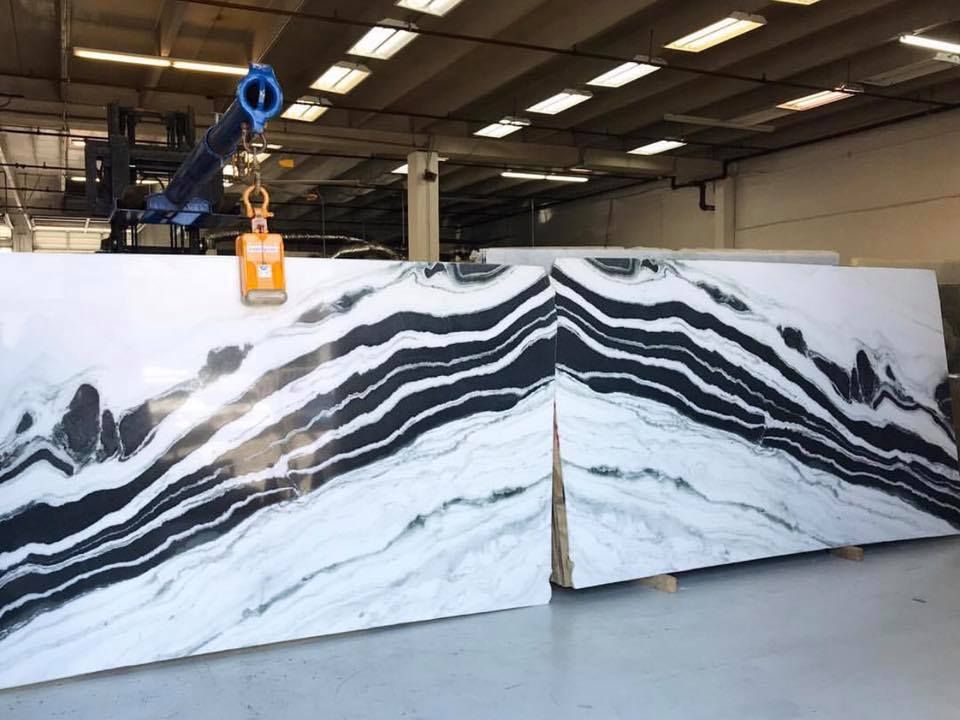 Large slabs of marble with black and white veining being moved by an overhead crane in a warehouse