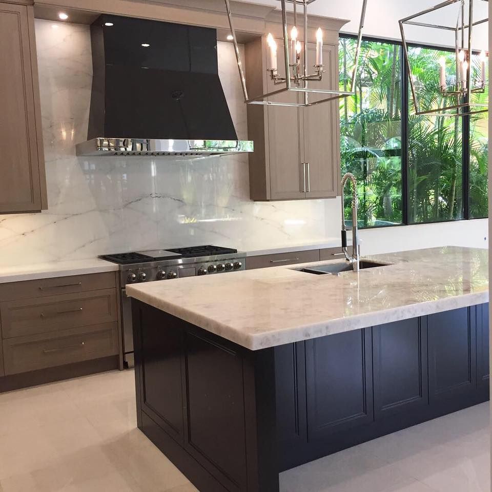 Modern kitchen with dark island, beige cabinets, stainless steel appliances, and marble backsplash