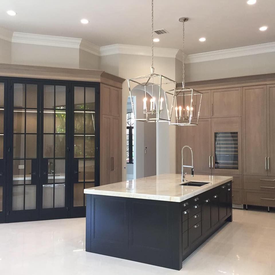 Modern kitchen with a black island, light-colored cabinets, and two geometric pendant lights