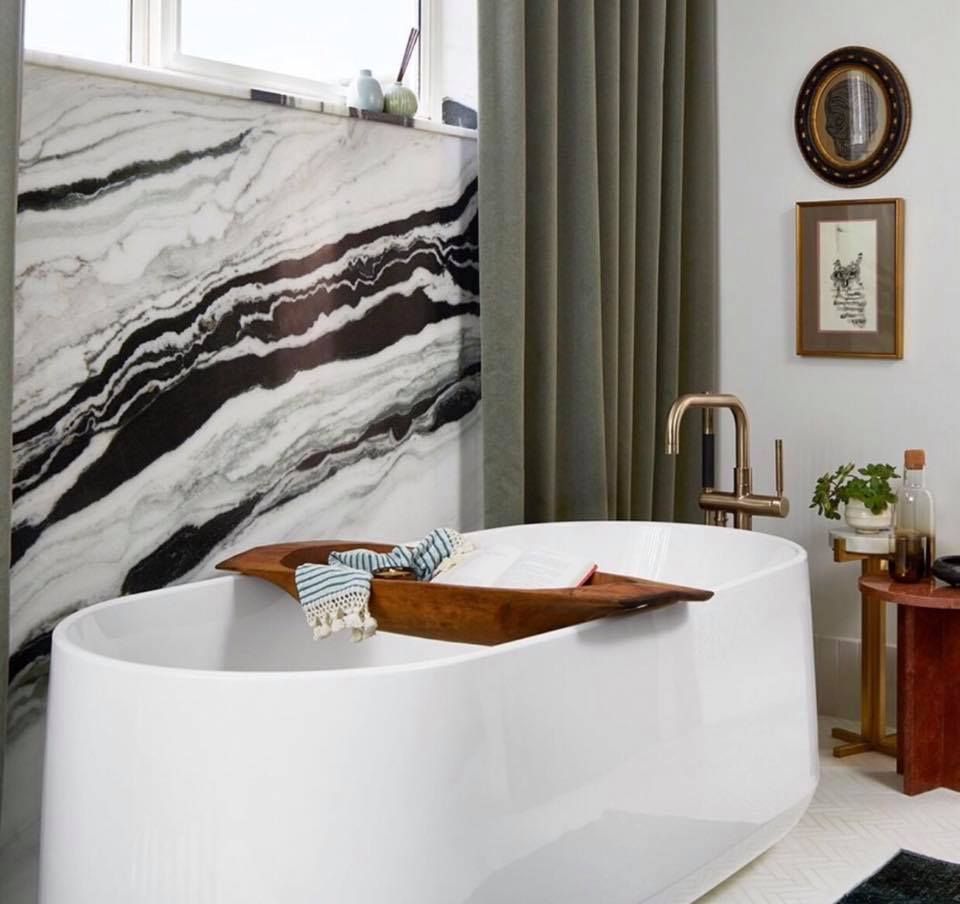 Luxurious bathroom with white tub, marble wall, gold faucet, and dark green curtains