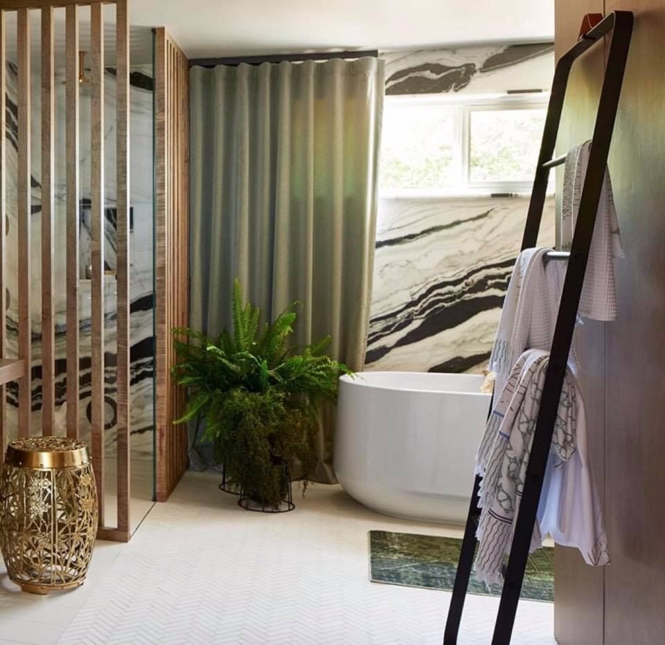 Bathroom with marble walls, a tub, greenery, a towel ladder, and wooden screen