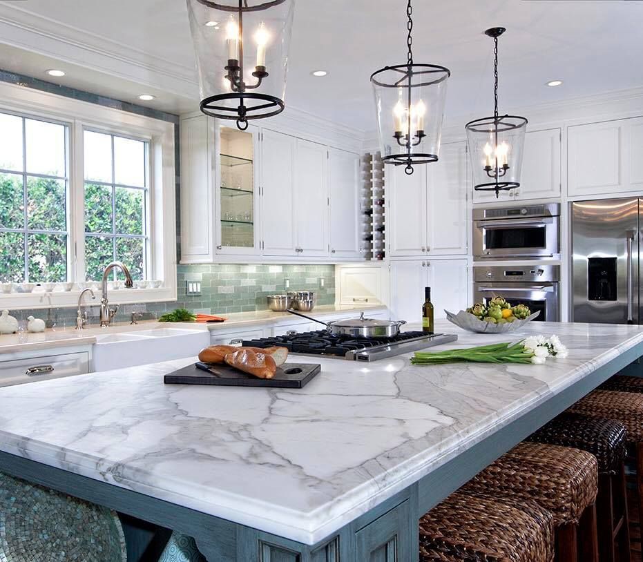 Elegant white kitchen with marble island, pendant lights, and woven bar stools