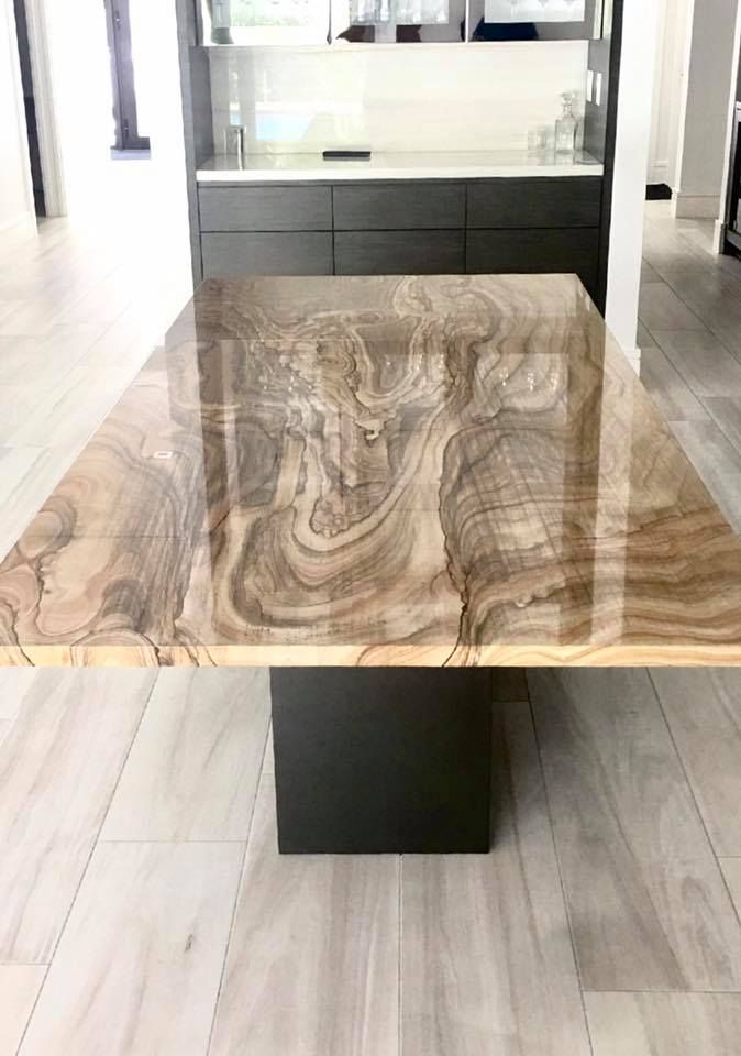 Wooden dining table with a swirling wood grain, supported by a dark square base