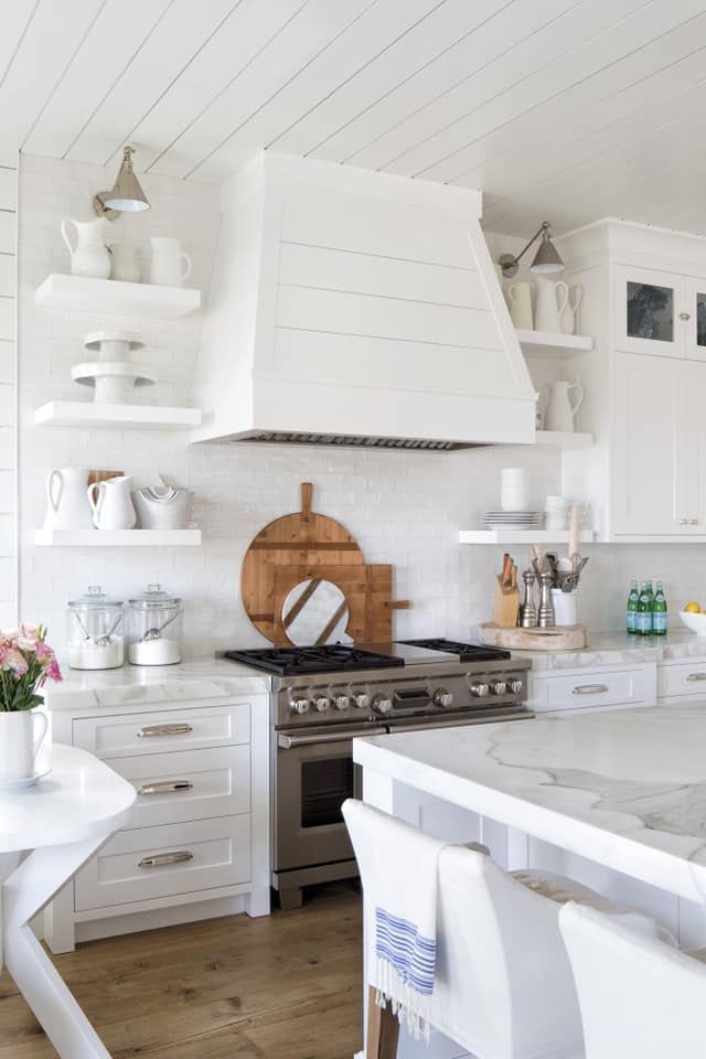 White kitchen with range, marble countertops, and open shelving with decor