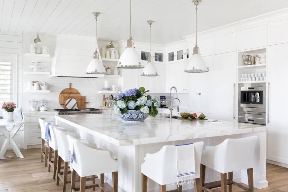 Bright white kitchen with island seating, overhead lights, and blue hydrangeas