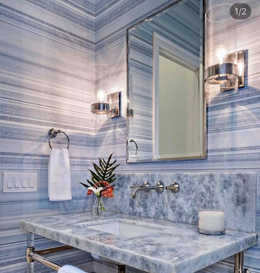 Blue and white striped wallpapered bathroom with marble sink, mirror, and sconce lighting