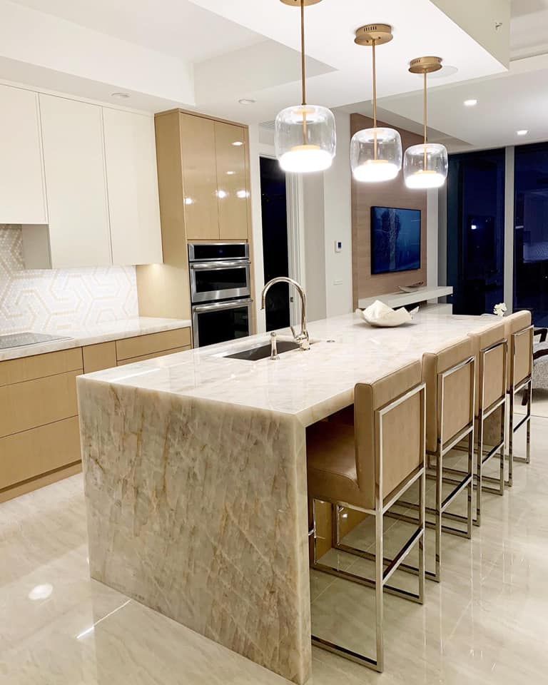 Modern kitchen with large island, light countertops, gold pendant lights, and beige cabinetry