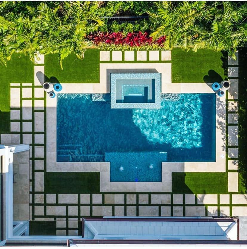 Overhead view of a rectangular pool and spa with lush green grass, stone tiles, and manicured landscaping