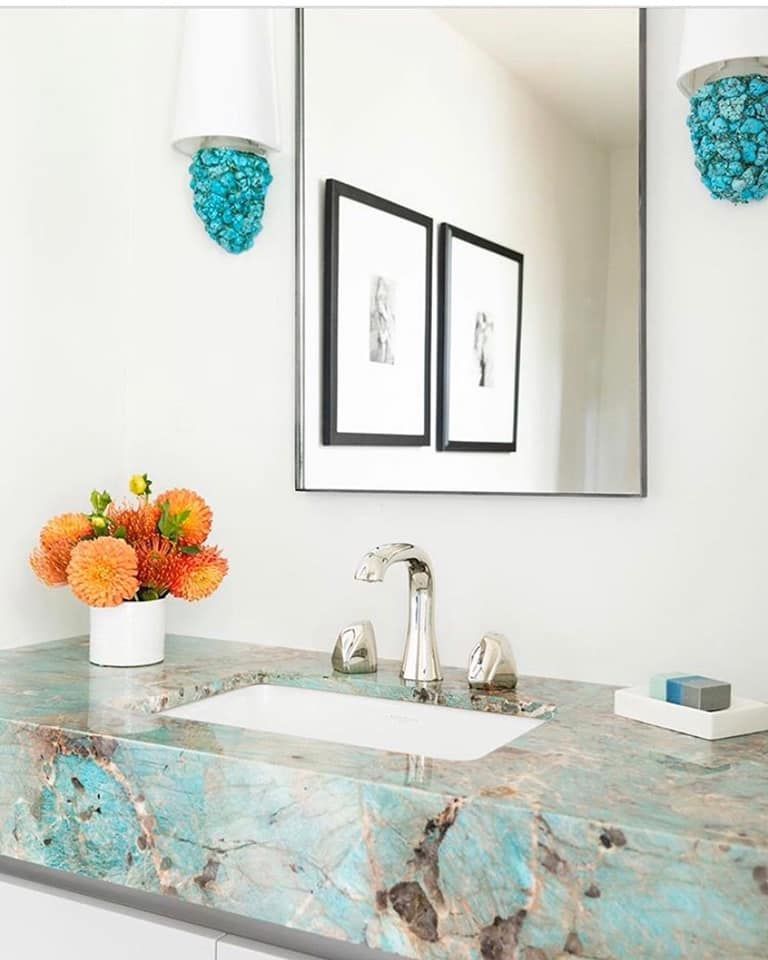 Bathroom with turquoise countertop, white sink, and framed art; orange flowers in a vase