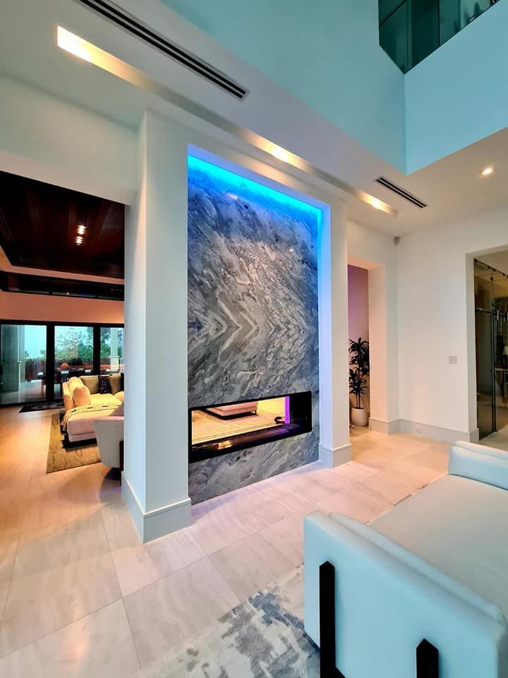 Modern fireplace with blue lighting, marble wall, and white accents in a luxurious home