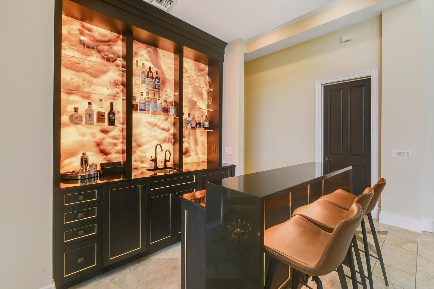 A home bar with a backlit marble display, black cabinets, and leather bar stools