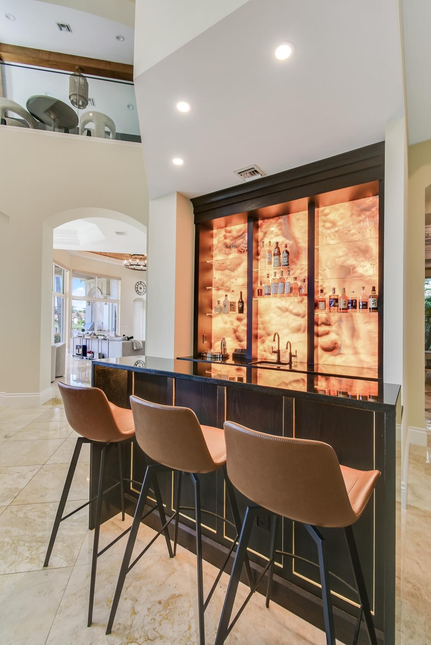 Bar with brown bar stools, dark bar, and backlit liquor display