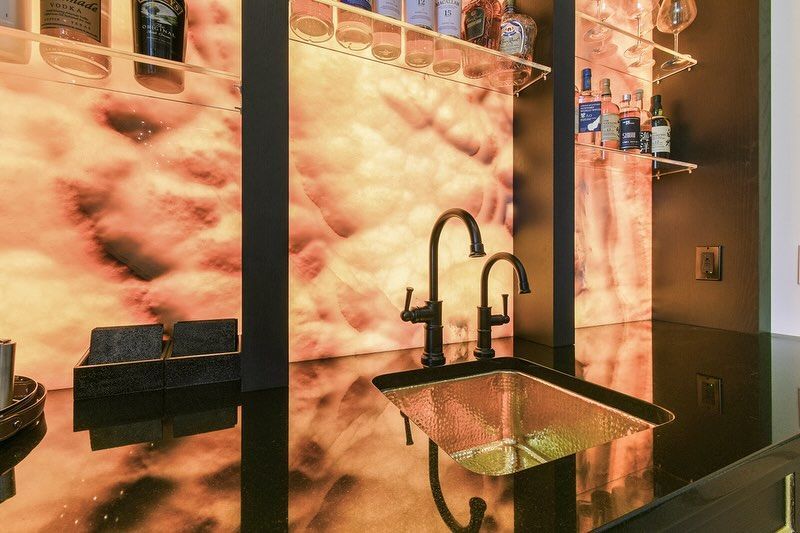 Bar with copper sink, black faucet, and backlit textured orange and white panel