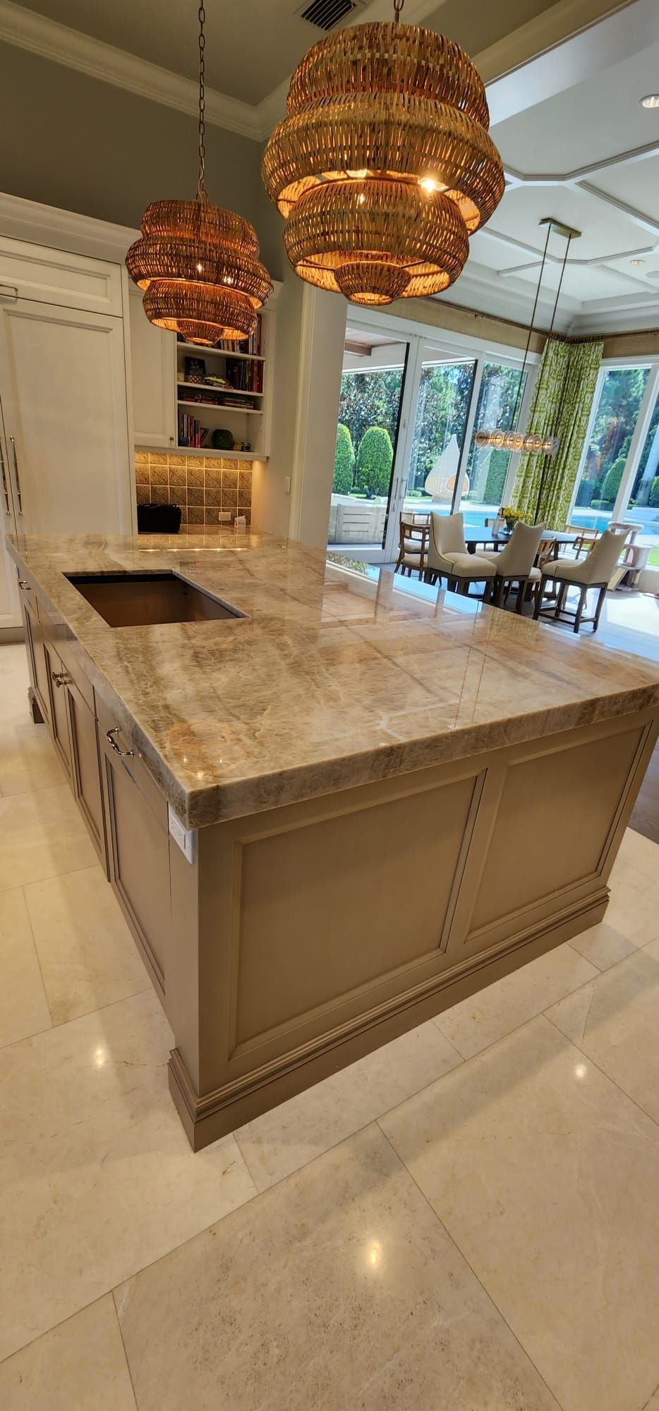 Kitchen island with patterned countertop, two globe lights, and view of outdoor dining