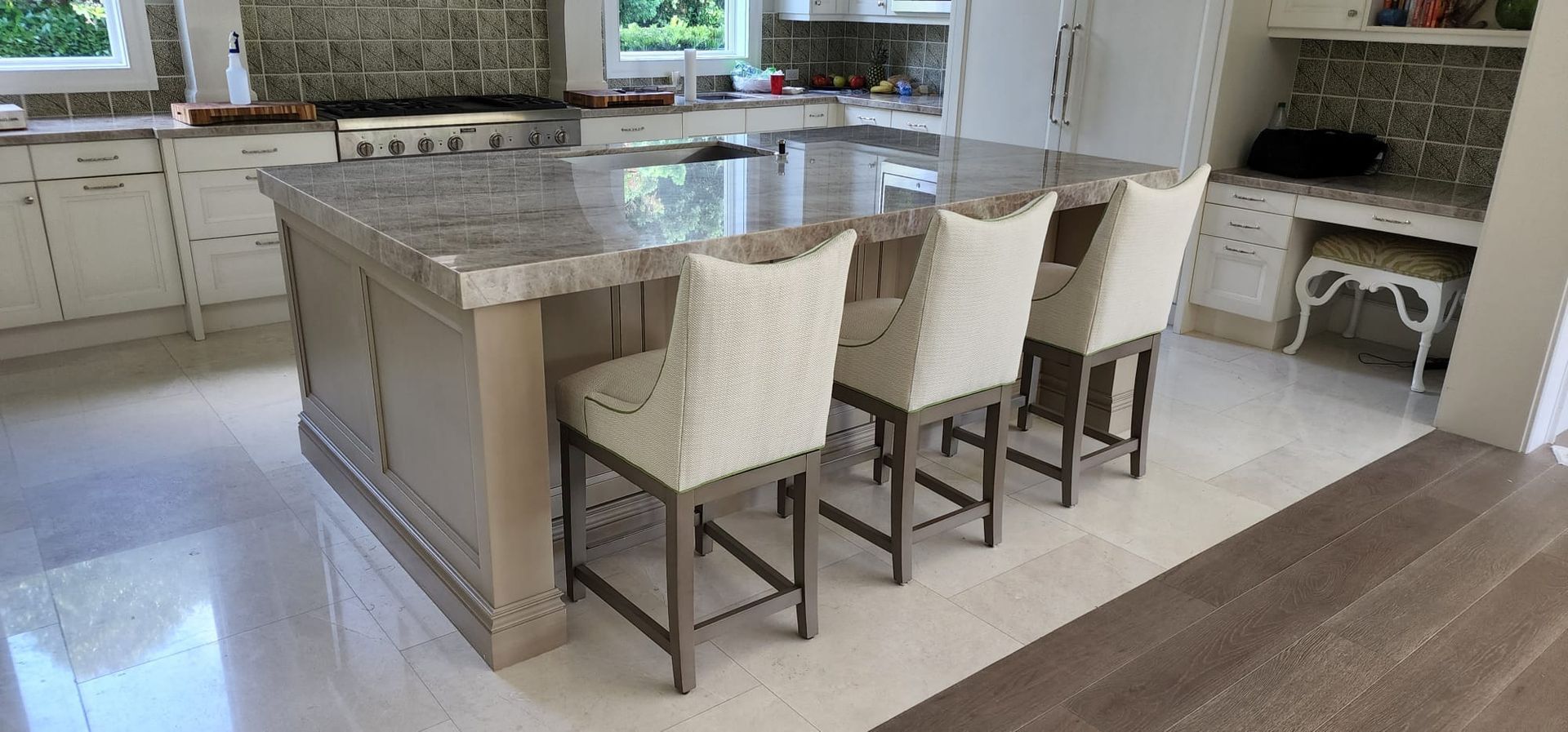 Kitchen with a large island, gray cabinetry, granite countertop, and four upholstered bar stools
