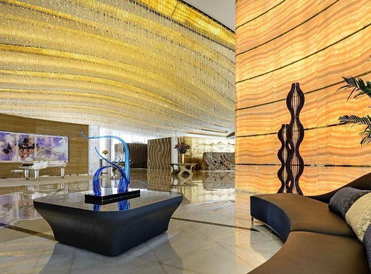 Hotel lobby with a large chandelier, modern furniture, and decorative onyx wall