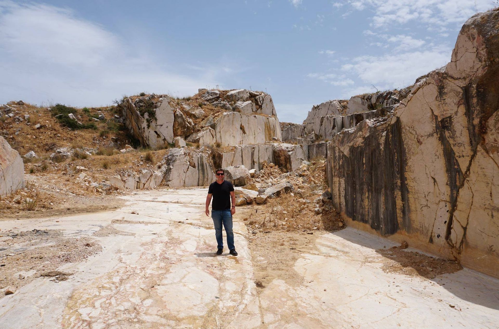 Man stands in a marble quarry. White rock faces surround, blue sky above