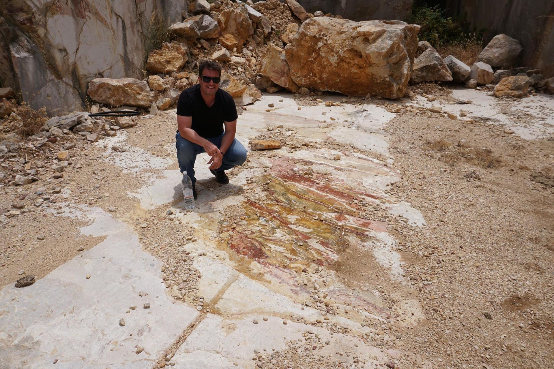 Man squats by colorful streaks on a rock surface in a quarry