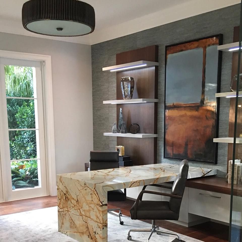 Modern home office with marble desk, shelves, artwork, and window with garden view