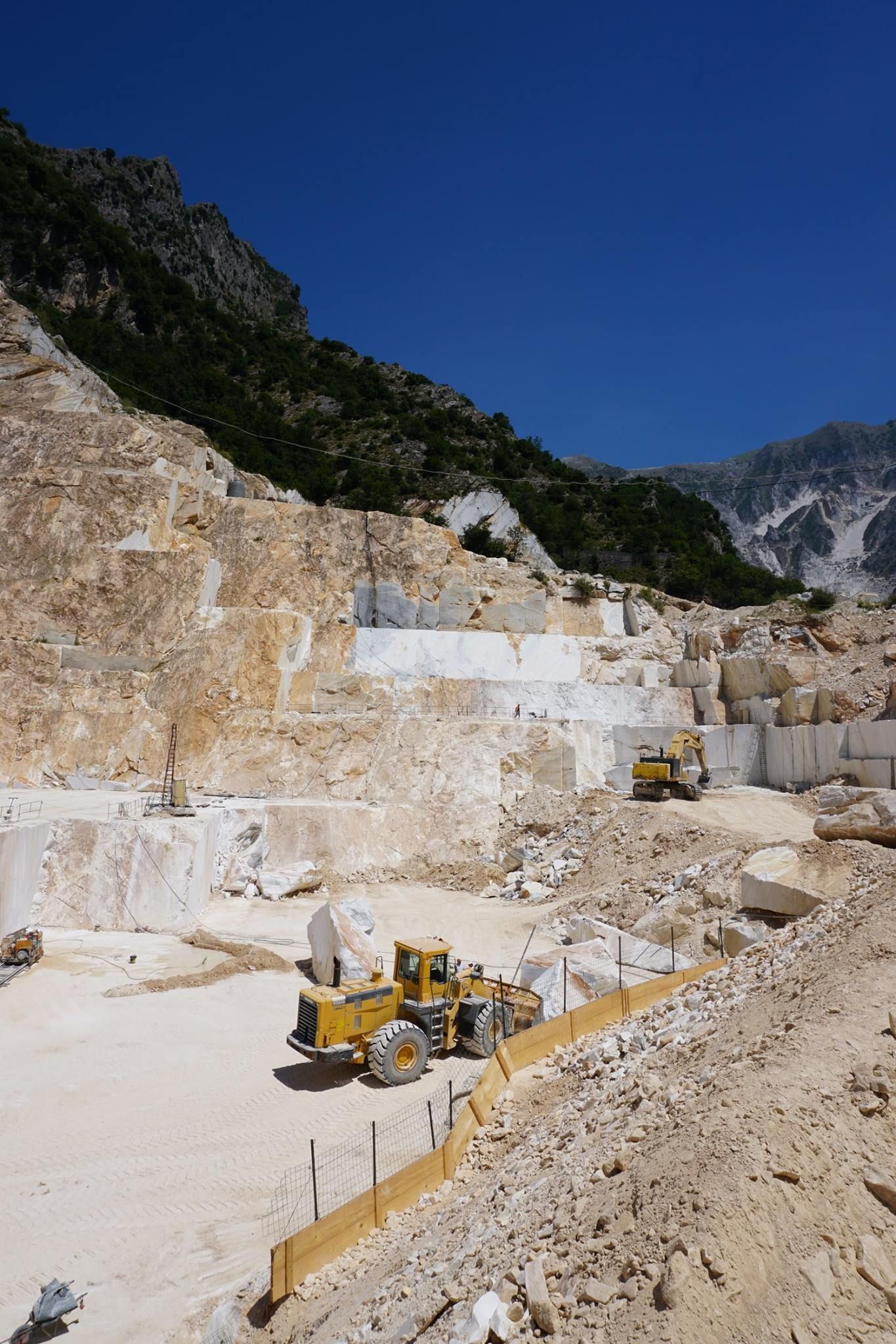 Marble quarry with yellow machinery; mountain backdrop, clear blue sky