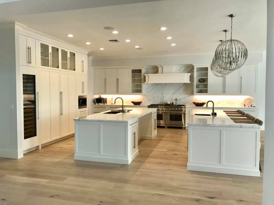Bright white kitchen with two islands, marble countertops, light wood floor, and a large chandelier