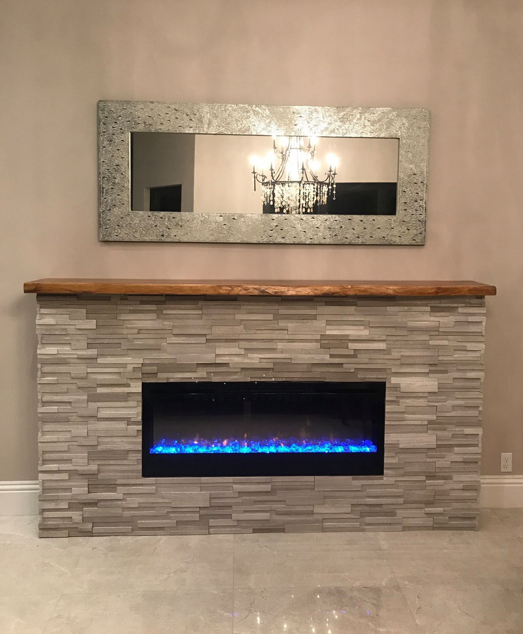 Fireplace with blue flames, gray stone, wood mantle, and mosaic mirror