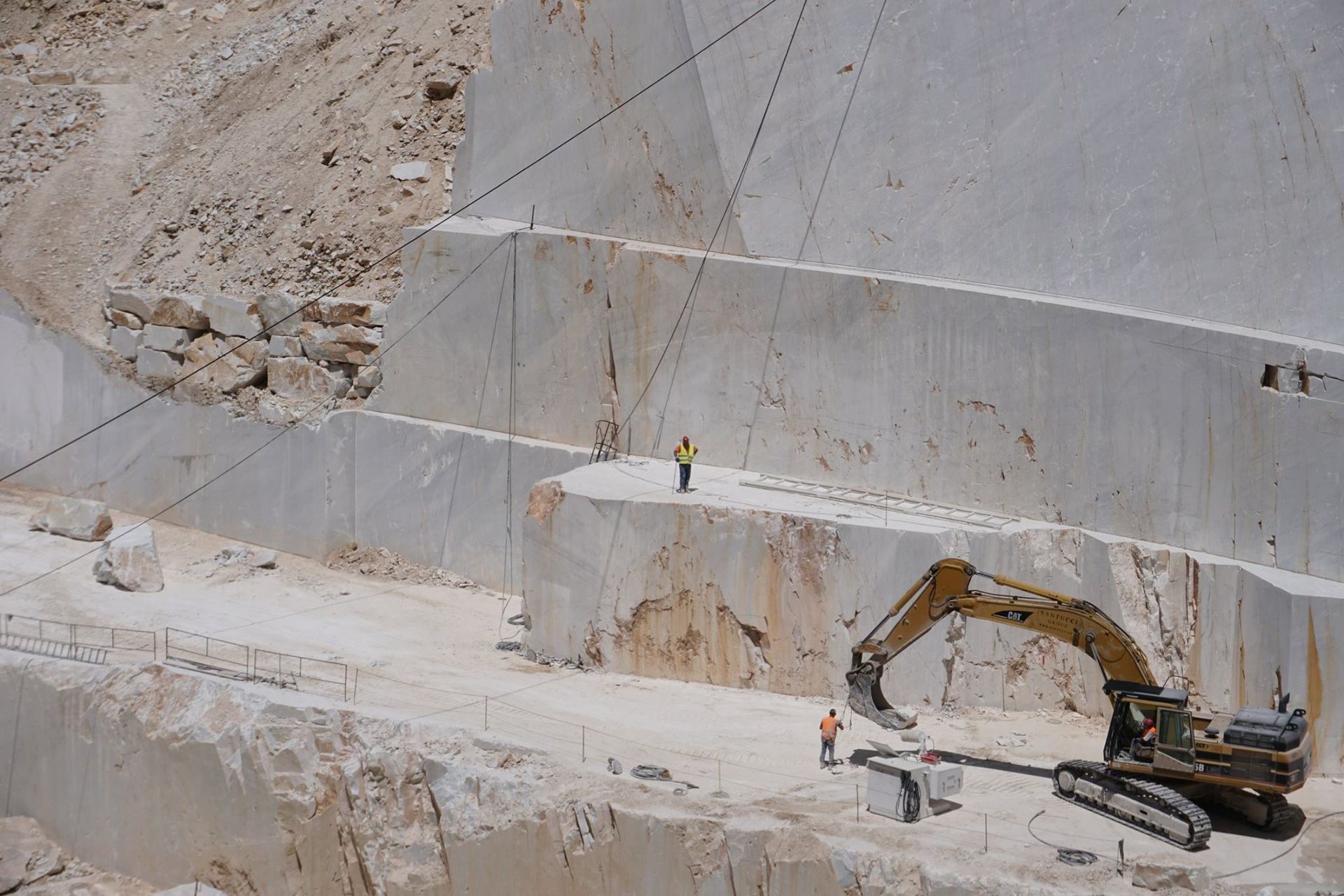 Marble quarry, workers, and excavator at work, cutting into a white marble cliffside
