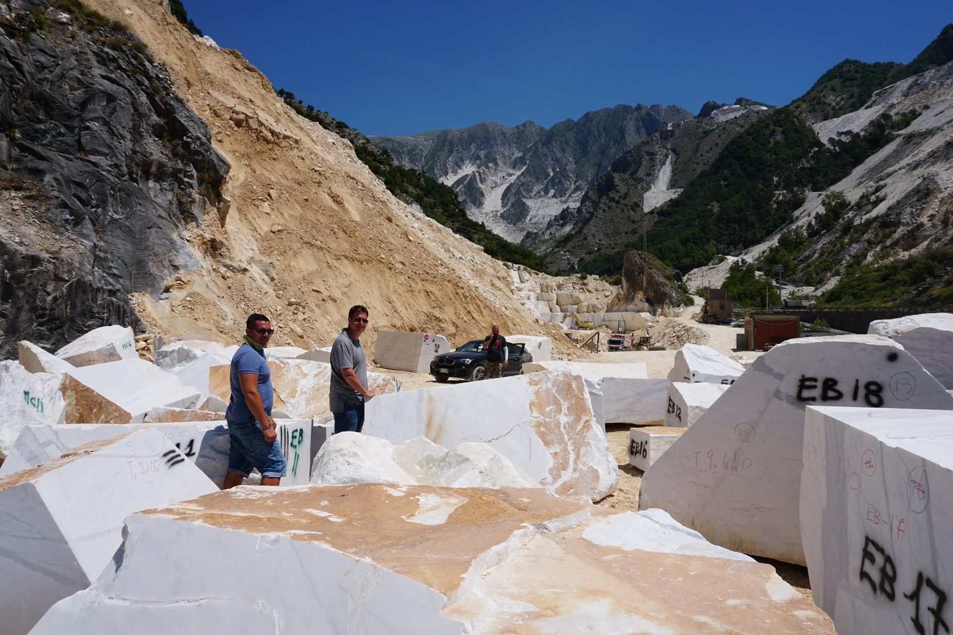 Two men and a car in a marble quarry with white blocks and mountains