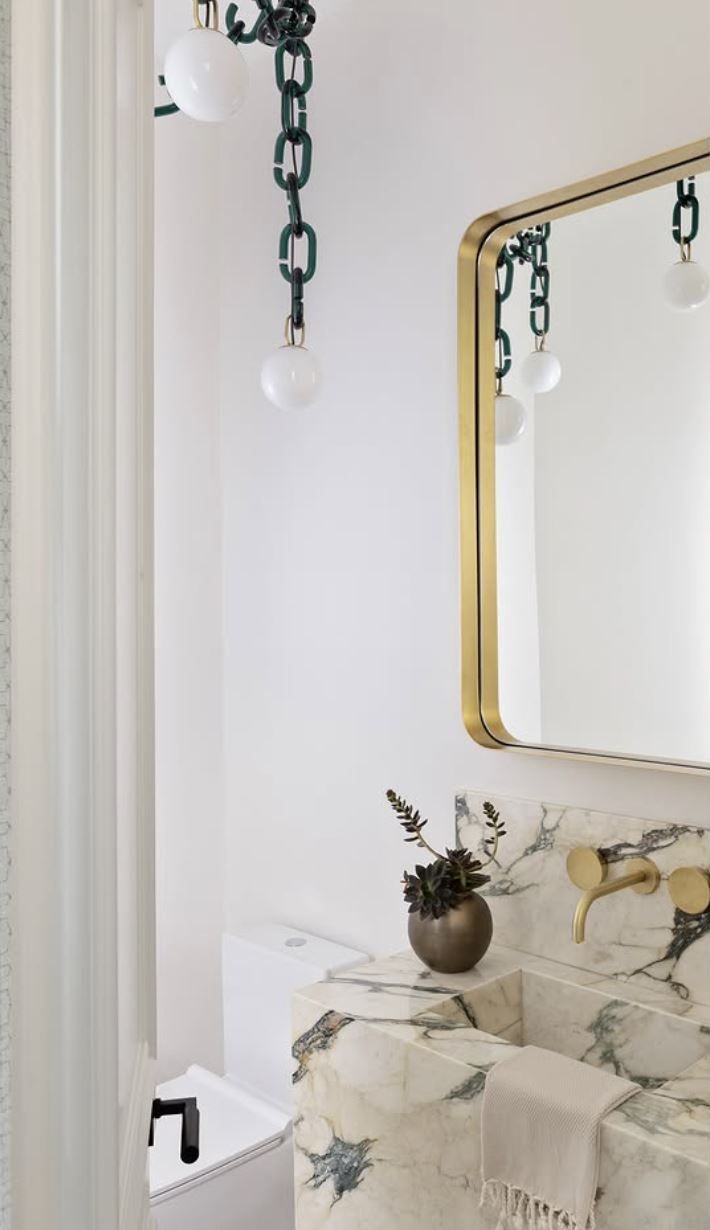 Bathroom with gold-framed mirror, marble sink, patterned fabric, and chain-linked lights