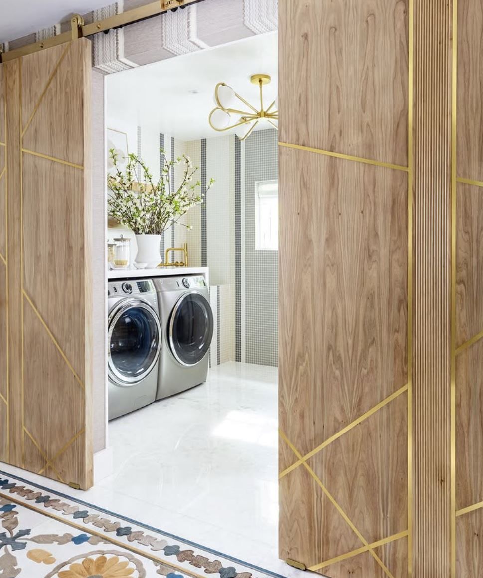 Wooden sliding doors with gold accents lead into a laundry room with silver appliances and white floor