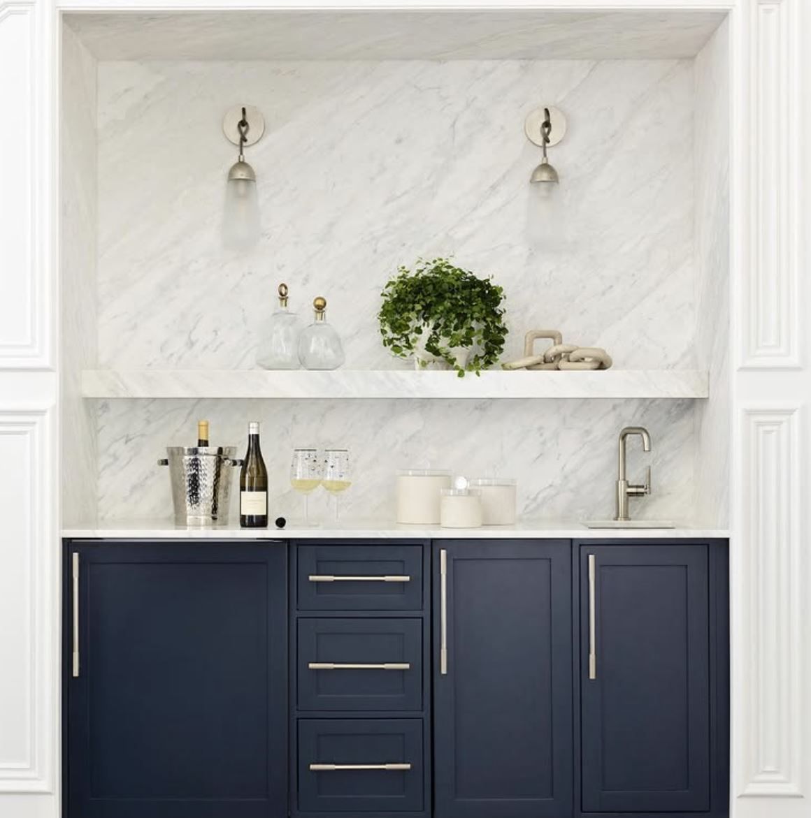 Built-in navy bar with white marble backsplash, shelving, silver accents, and greenery