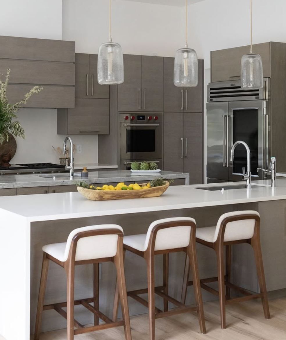 Modern kitchen with grey cabinets, white countertop island, and three bar stools