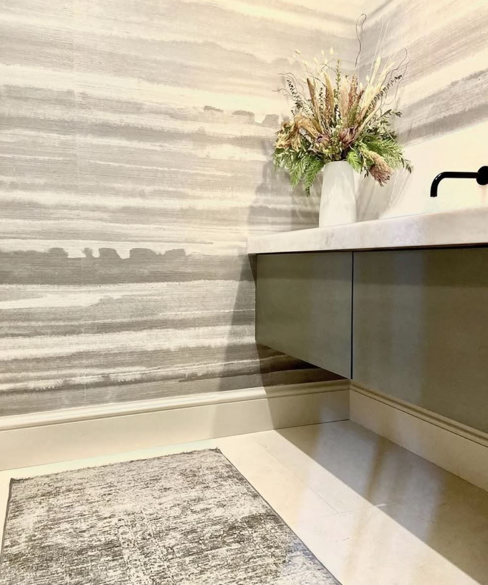 Bathroom with gray patterned wallpaper, floating sage cabinet, white countertop, and floral arrangement