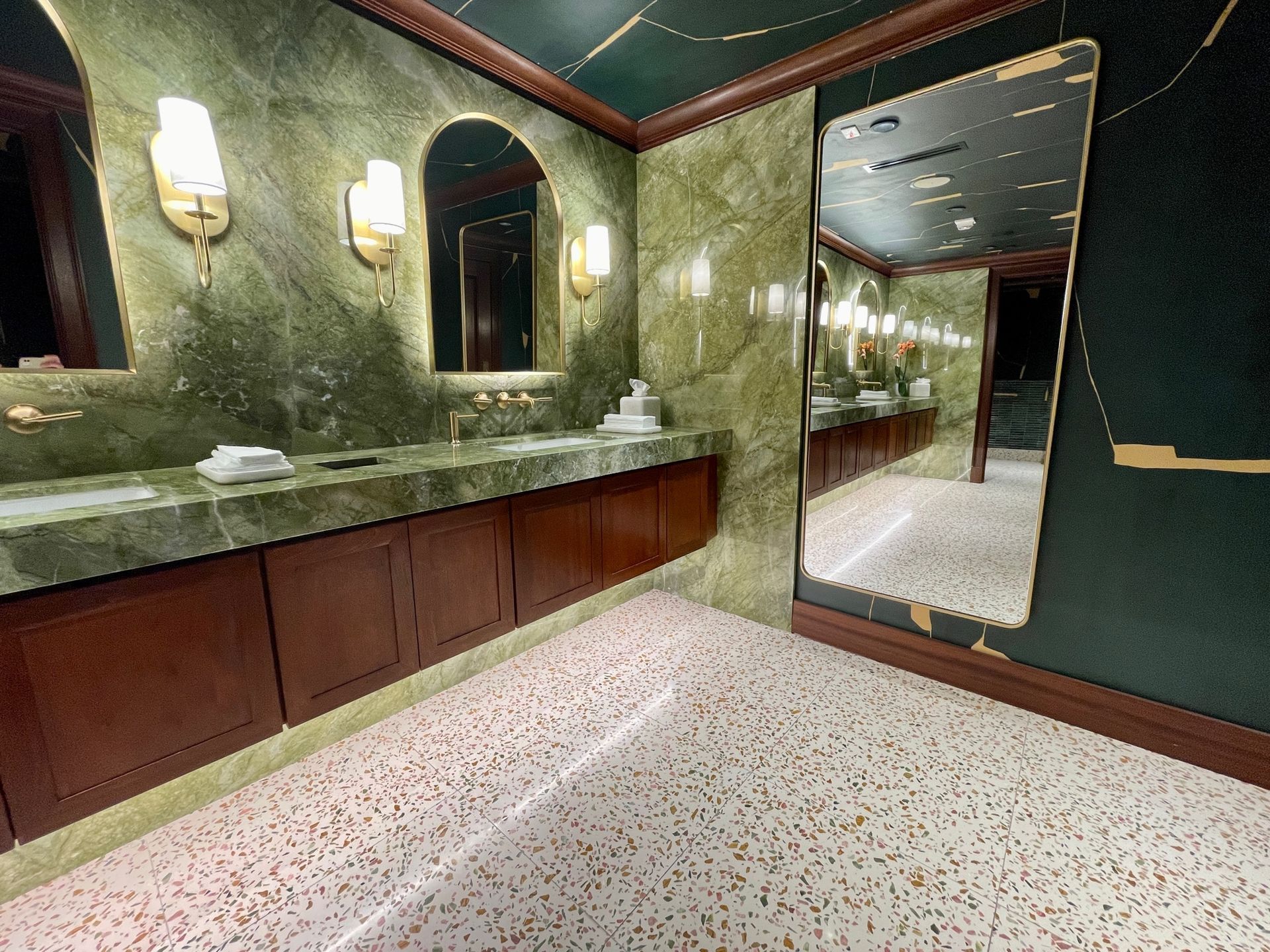 Luxurious green marble bathroom with gold accents, large mirror, and brown cabinets
