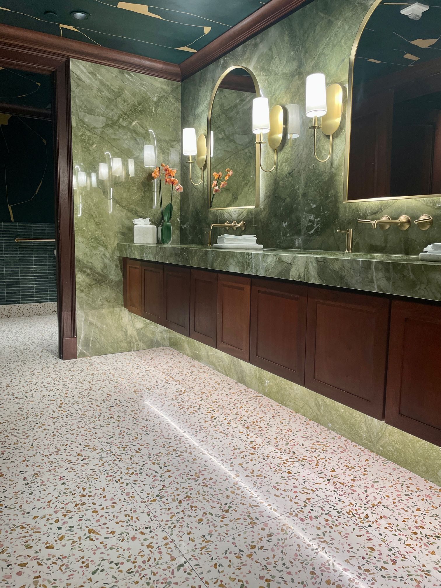 Luxurious bathroom with green marble walls, wooden cabinets, and terrazzo floors