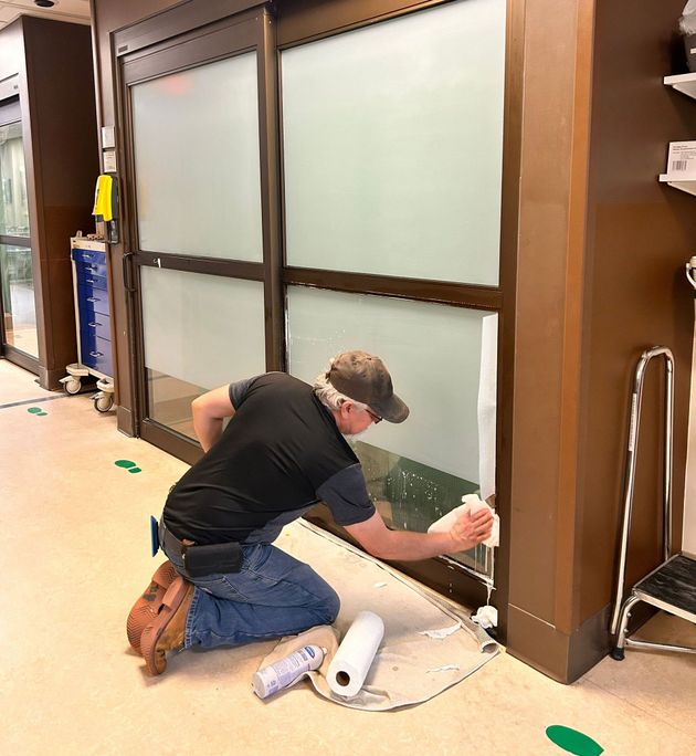 Person kneeling to paint a large frosted window frame in an indoor workspace