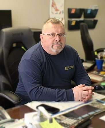 Man seated at an office desk, wearing glasses and a navy shirt, with a neutral expression.