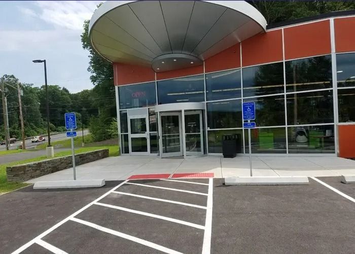 Modern building entrance with glass doors, red and gray facade, and accessible parking spaces in front