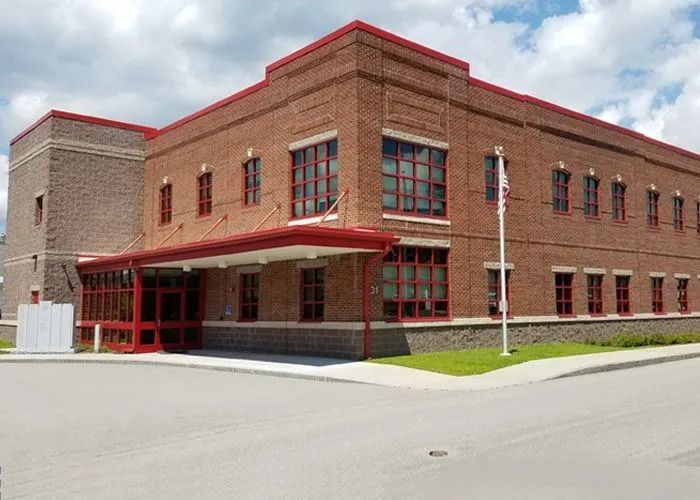 Brick building with red trim and large windows, viewed from a street corner under a cloudy sky.