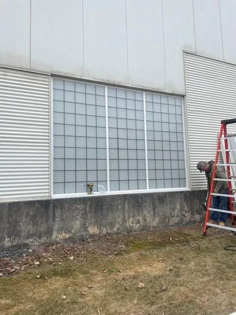 Building exterior with glass-block windows, concrete foundation, grass, and a red ladder on the right.