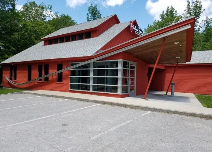 Red building with angled roof and glass entrance beside an empty parking lot