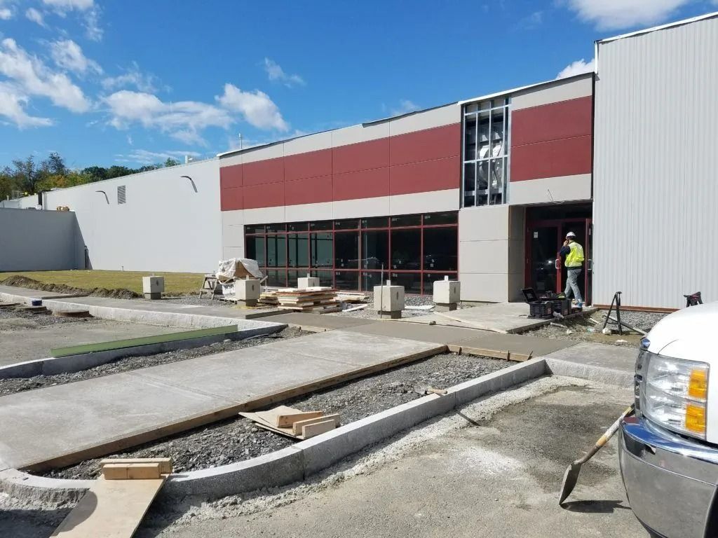 Construction site outside a new storefront with workers, concrete curbs, and a red-and-white facade
