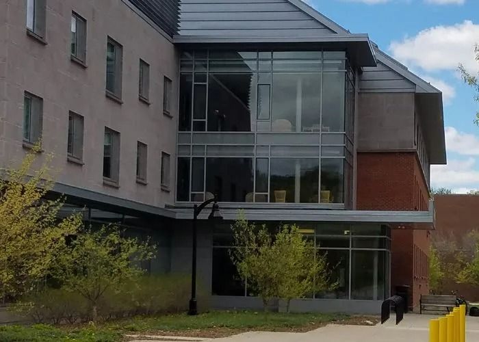 Modern building entrance with glass facade, overhanging roof, and a person walking near the doorway