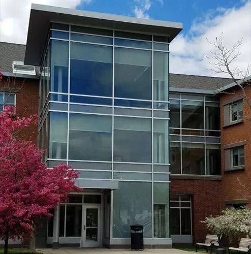 Modern glass-front building entrance with brick wings, trees, and a cloudy sky