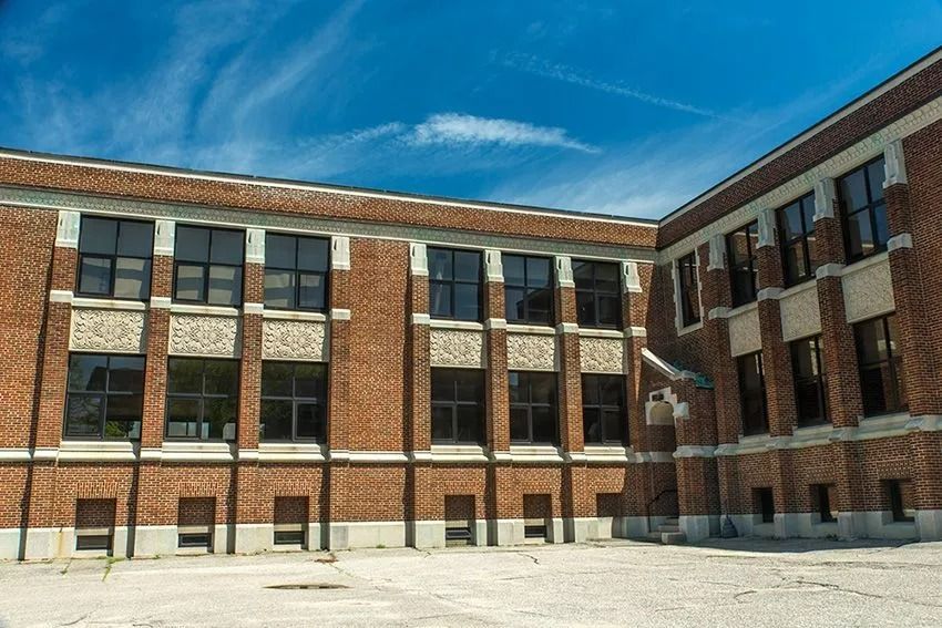Brick school building with rows of windows under a bright blue sky