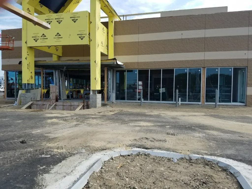 Construction site with yellow steel framework beside a glass storefront and dirt foreground