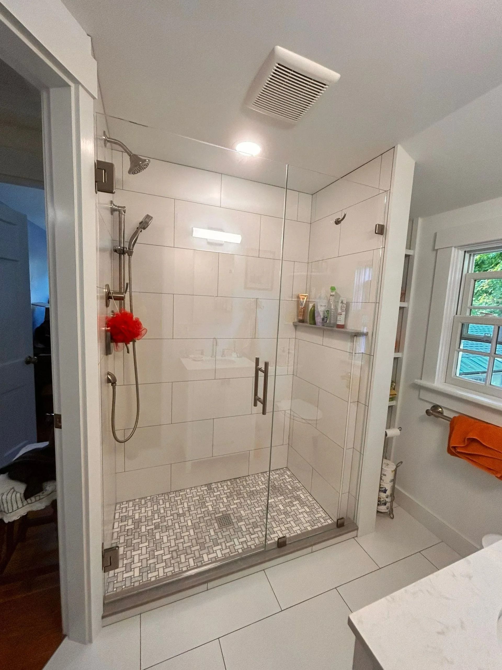 Modern white-tiled bathroom with walk-in shower, mosaic floor, glass door, and wall-mounted shower fixtures