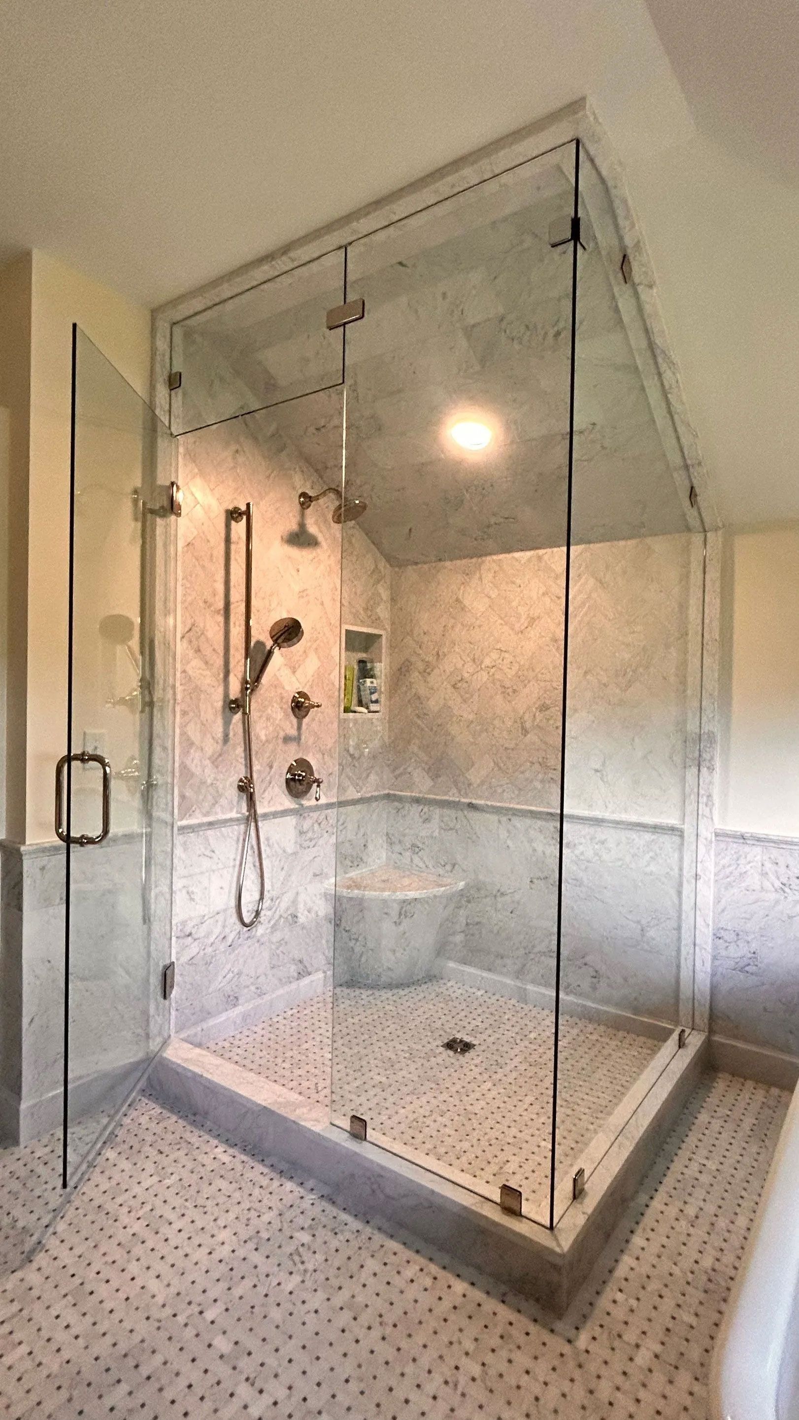 Glass-enclosed walk-in shower with marble tile, dual shower heads, and a built-in bench
