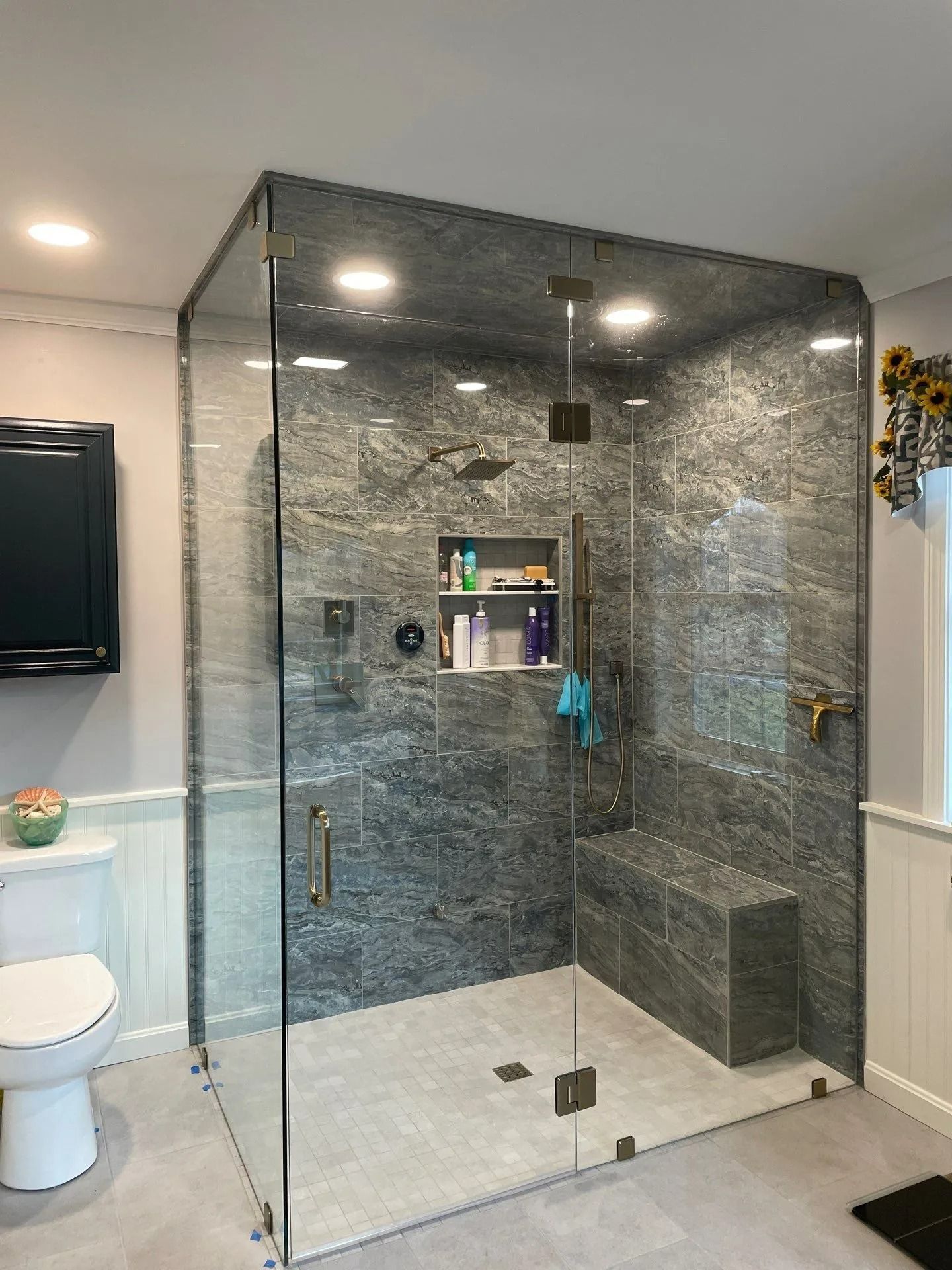 Modern bathroom with a glass walk-in shower, dark tile walls, and a white toilet beside it.