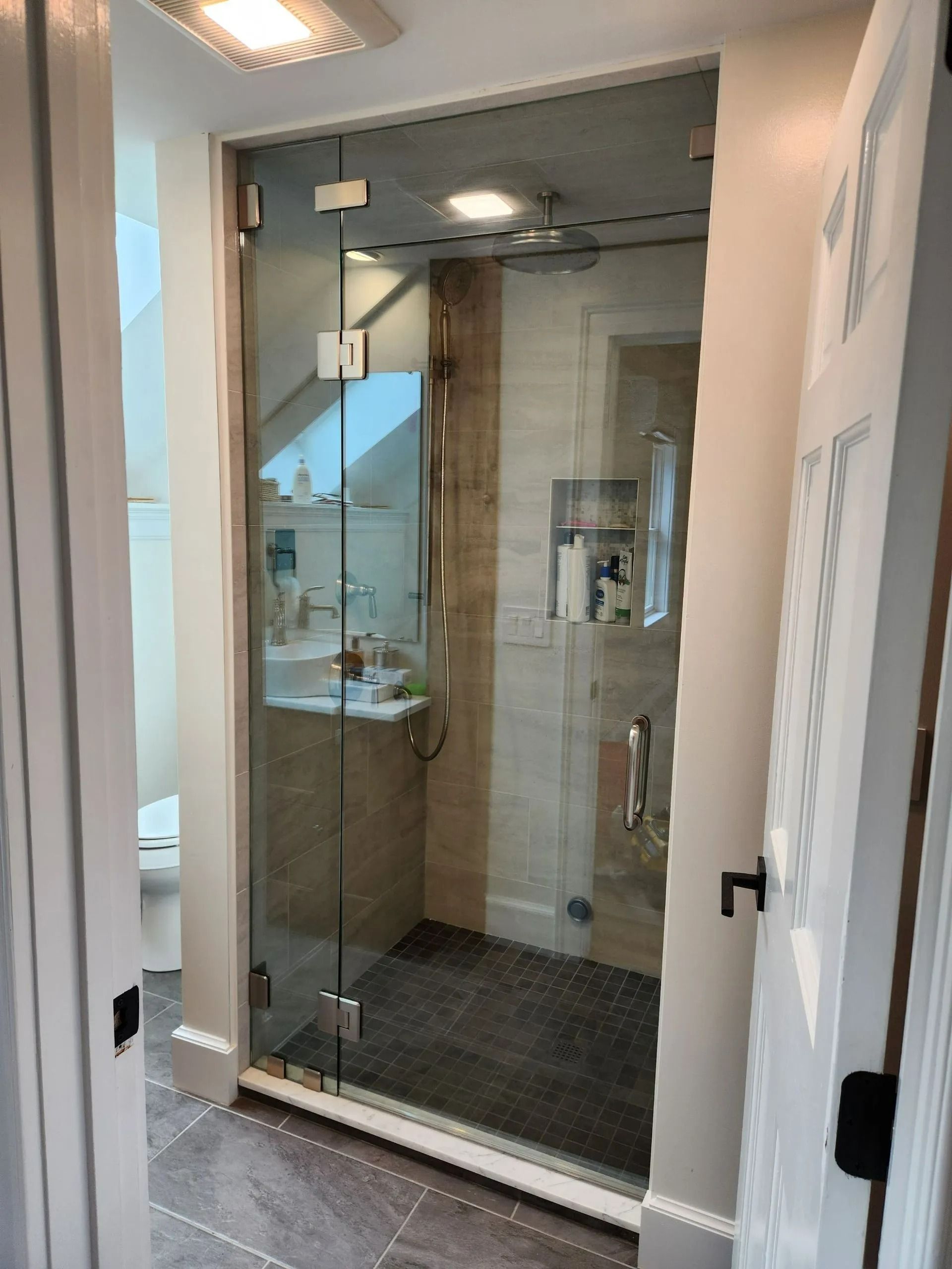 Glass shower stall with chrome fixtures and dark tile floor in a bathroom